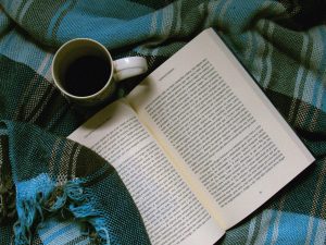 A book and a coffee on a blue plaid blanket.